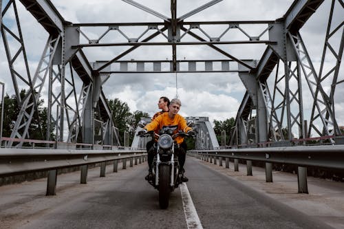 A Man in Orange Jacket Riding Motorcycle on Bridge