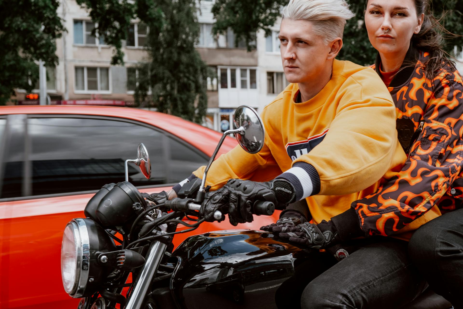 A couple in vibrant attire rides a motorcycle on a city street, showcasing urban adventure.