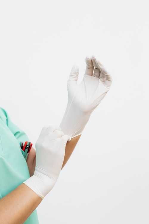 Free A healthcare worker in green scrubs wearing white surgical gloves, preparing for procedure. Stock Photo