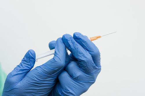 Free Close-up of blue gloved hands holding a syringe needle ready for injection. Stock Photo