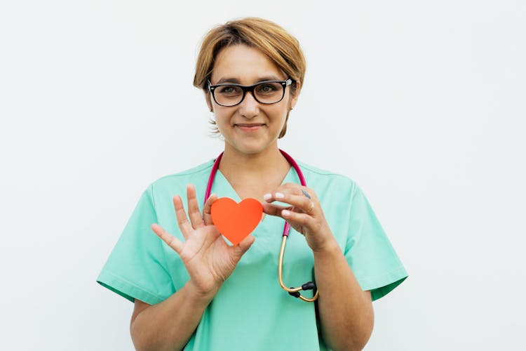 A Doctor Holding A Heart Paper Cutout And Smiling 