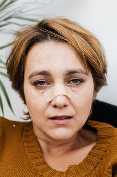 特写镜头中，一名白人妇女鼻子上贴着创可贴，神情悲伤，流露出痛苦