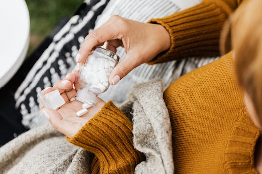 Close-up of a person holding a glass bottle with white pills, captured indoors.