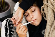 一名妇女裹着舒适的毯子躺在沙发上，用温度计测量体温