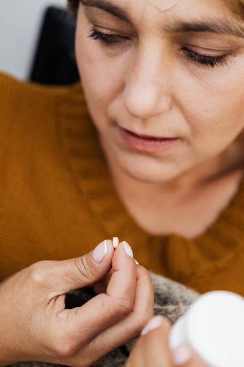 Free Close-up of a woman holding pills, wearing a knitted sweater, conveying health and care. Stock Photo