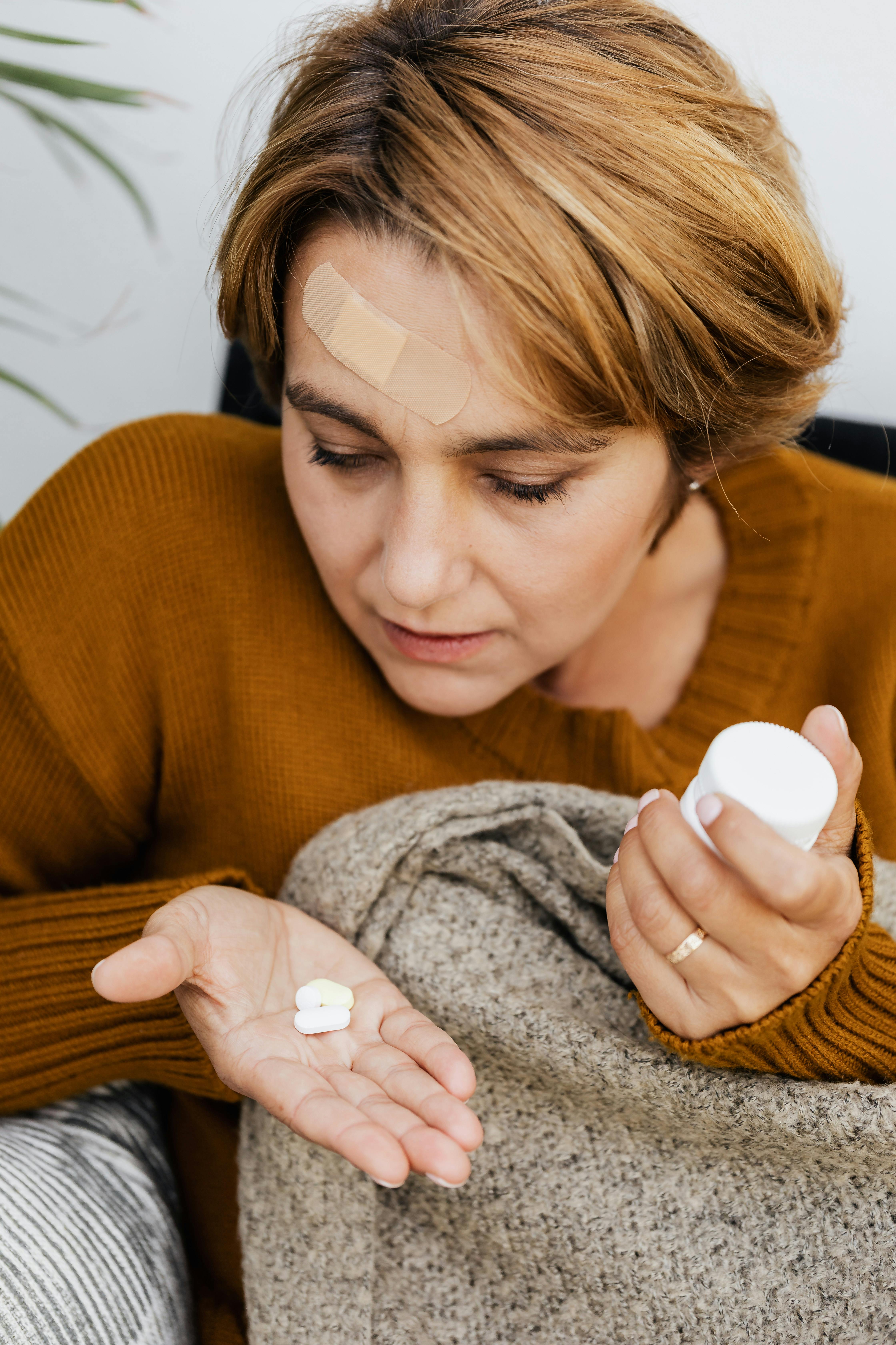 头上缠着绷带的妇女，手里拿着药丸和药瓶，代表着家里的医疗保健