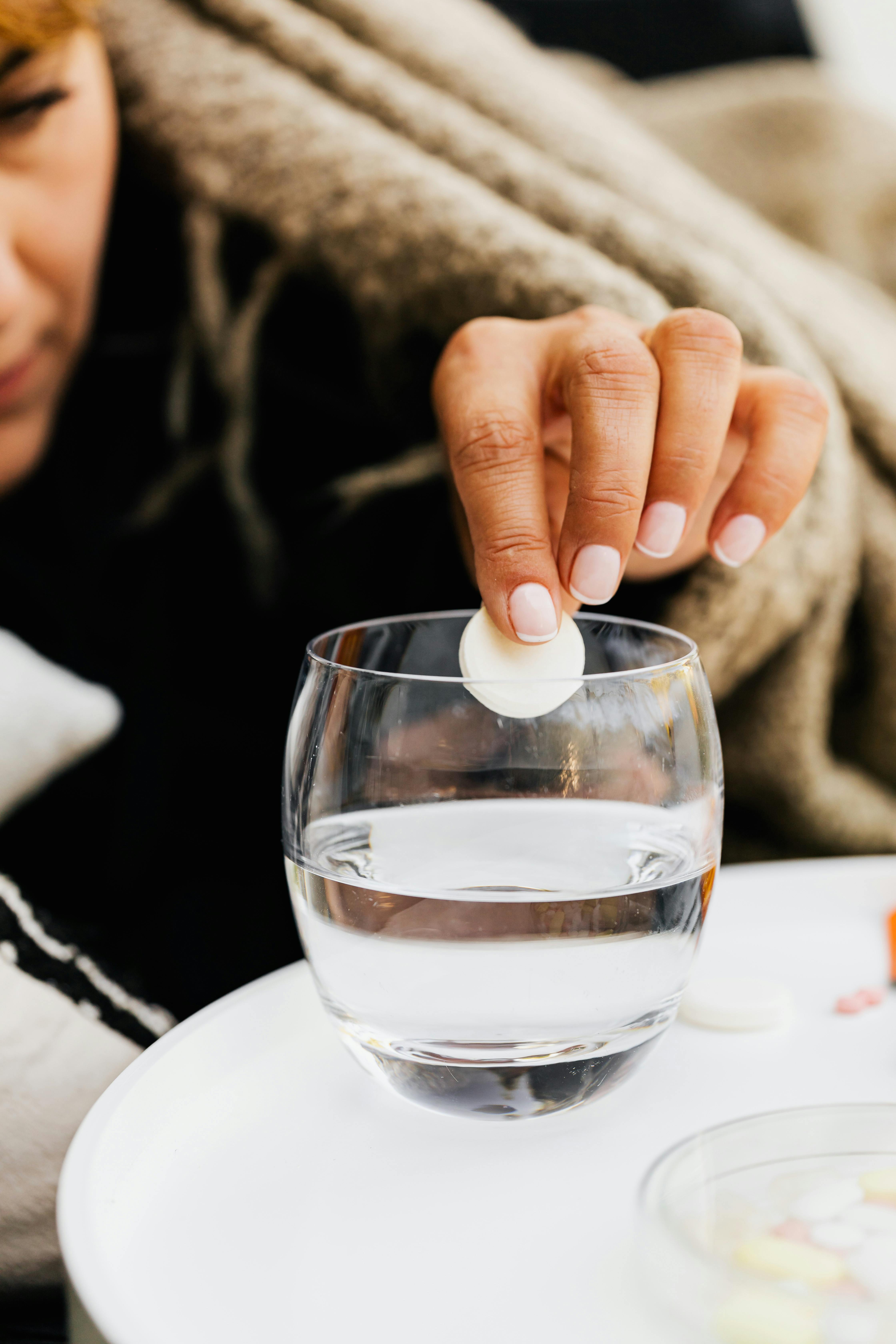 Close-up of hand dropping effervescent tablet in glass of water on table.