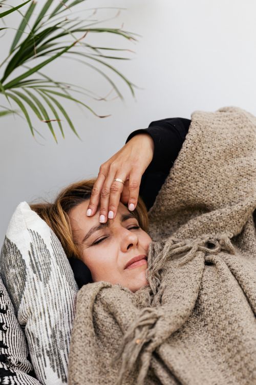 Free A woman resting indoors, appearing unwell with a headache, under a warm blanket. Stock Photo