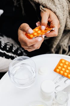 Close-up of hands handling blister pack with yellow pills. Includes glass of water on table.