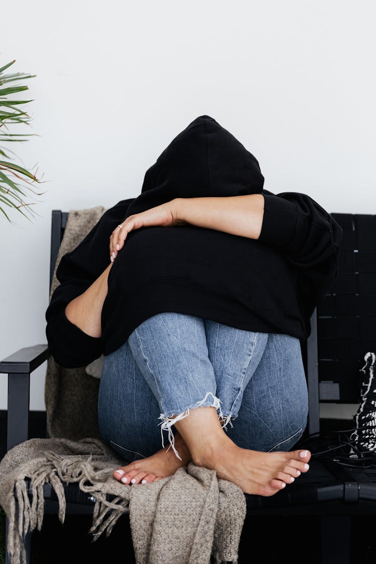 
A Person In A Black Hoodie Curled Up On A Couch