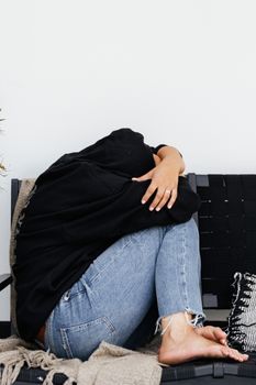 室内，一个人蜷缩在黑暗的沙发上，显露出压力和悲伤的迹象