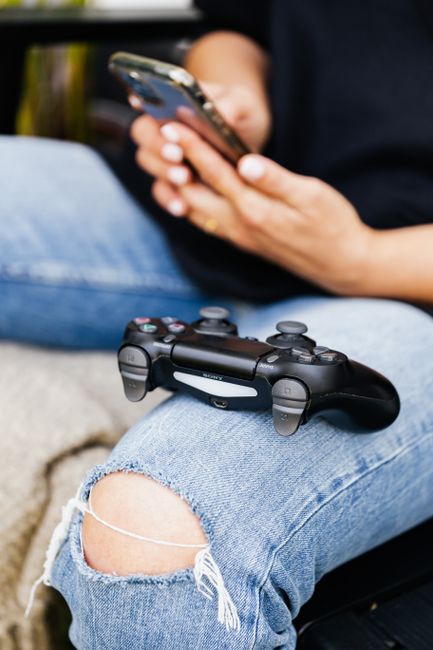 Person relaxing with a smartphone and video game controller on denim pants.
