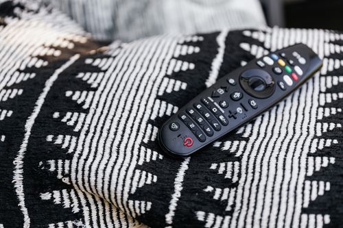 Free A black remote control resting on a monochrome patterned blanket, emphasizing modern home comfort. Stock Photo
