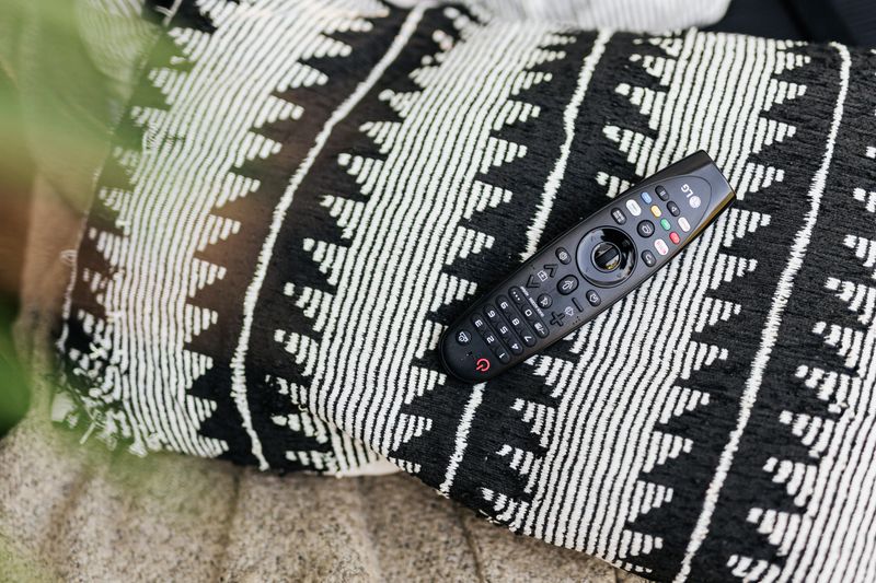 Close-up of a black remote control resting on a patterned throw pillow.