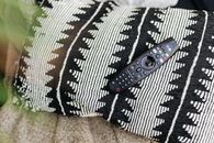 Close-up of a black remote control resting on a patterned throw pillow.
