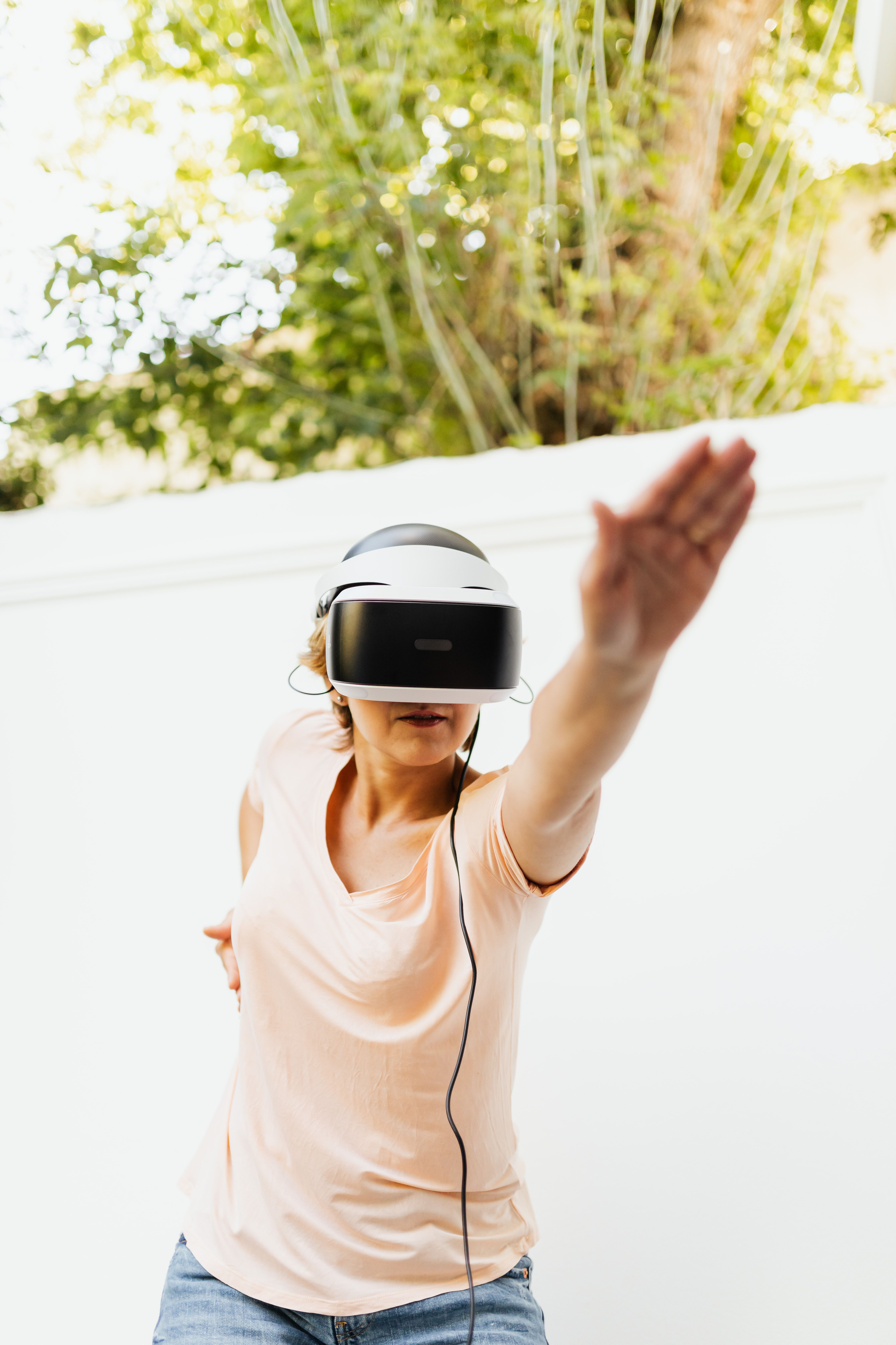 A woman using a VR headset outdoors, reaching upwards while engaging with virtual reality technology.