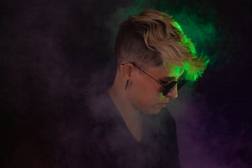 Free Side view of concentrated woman in stylish eyeglasses covered in smoke in dark room with bright light Stock Photo