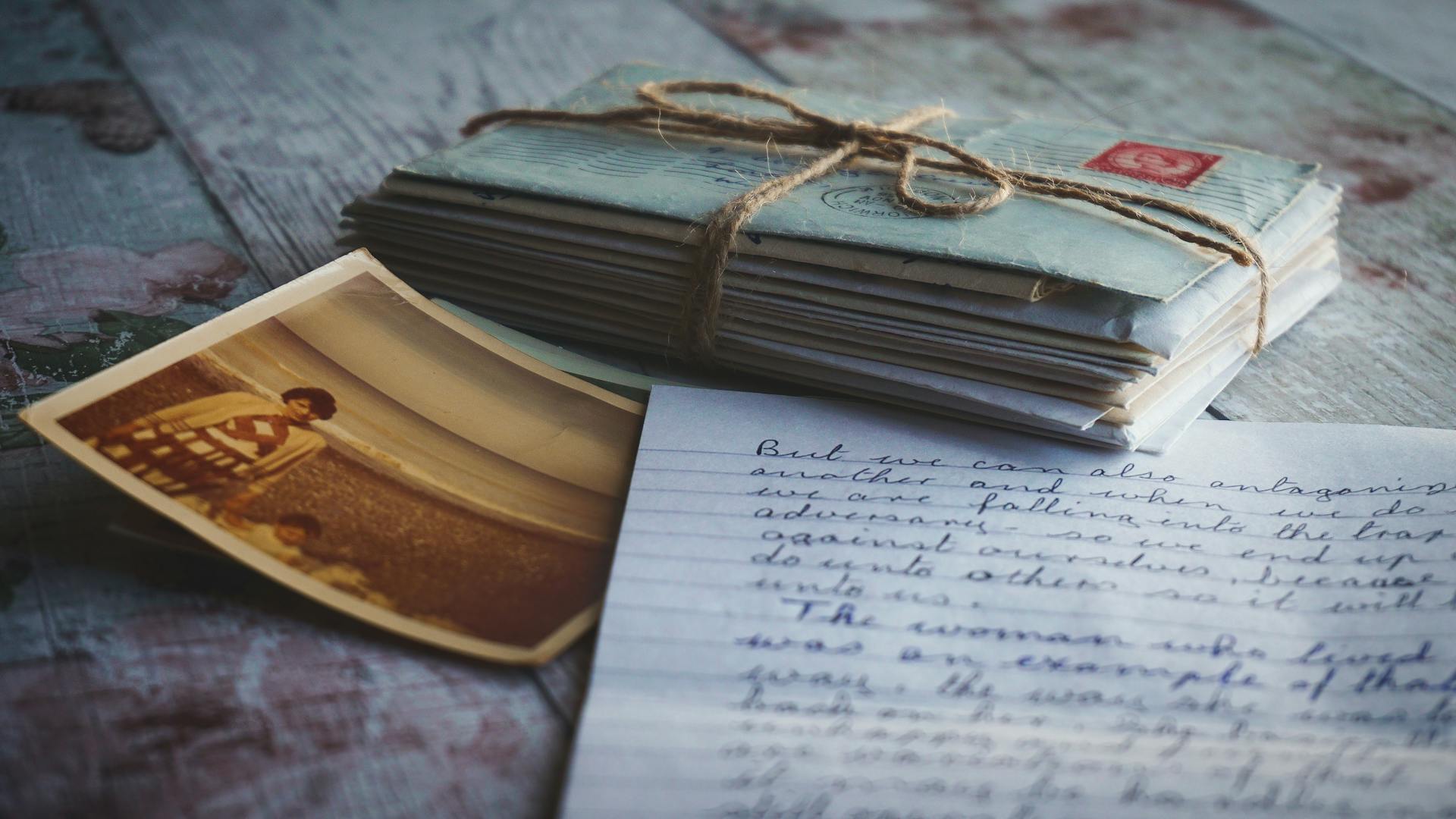 Stack of vintage letters tied with twine, a sepia photo, and a handwritten note on a wooden surface.