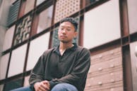 Thoughtful Asian man sitting near building