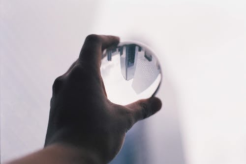 Crop anonymous person demonstrating transparent glass ball in hand against white wall with upside down reflection of modern tall skyscrapers in daylight