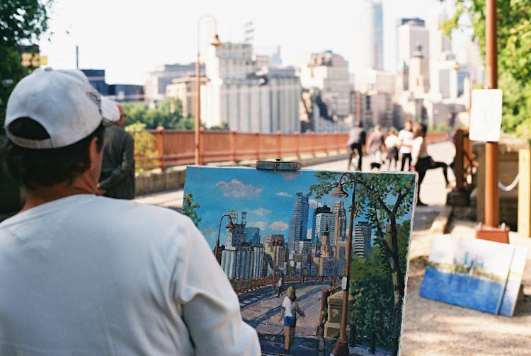 Unrecognizable Man Drawing On Easel In City