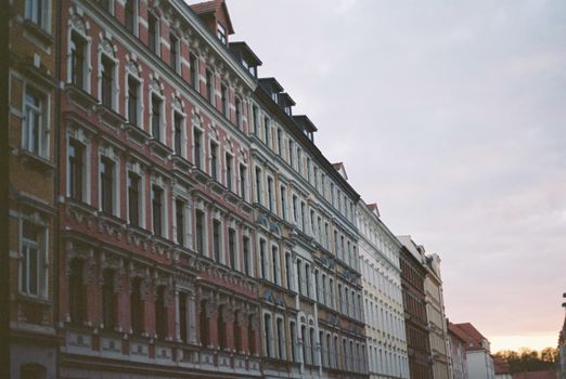Perspective view facade of aged multicolored building with ornamental windows arranged in evenly rows in city street at evening time