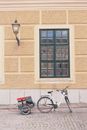Bicycle with trailer parked on pavement near house facade with window with black frame and lantern on painted brick wall
