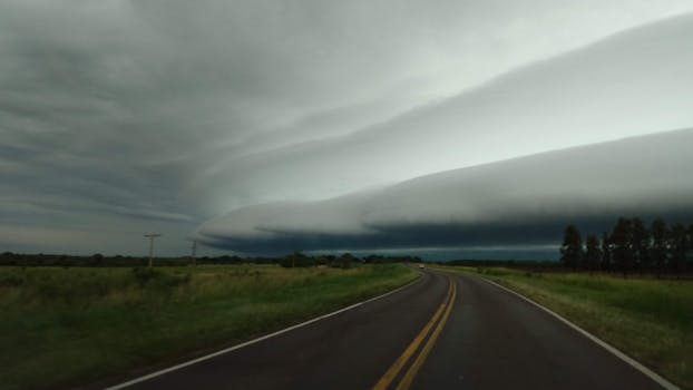 A dramatic formation of storm clouds stretches over an empty rural highway, creating a moody atmosphere.