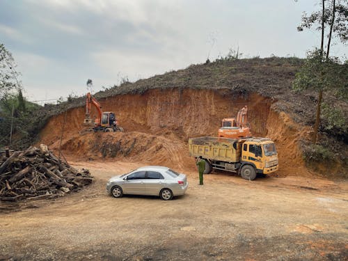 A Car, a Truck, and an Excavator Beside the Cliff