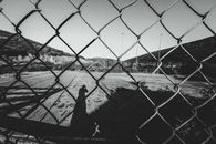 Through metal net fence of black and white sports ground surrounded by mountains on sunny day