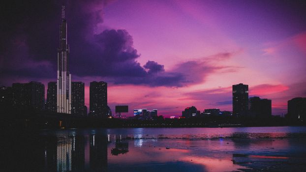 日落时分，当代摩天大楼的倒影映在城市河流中，天空多云却明亮
