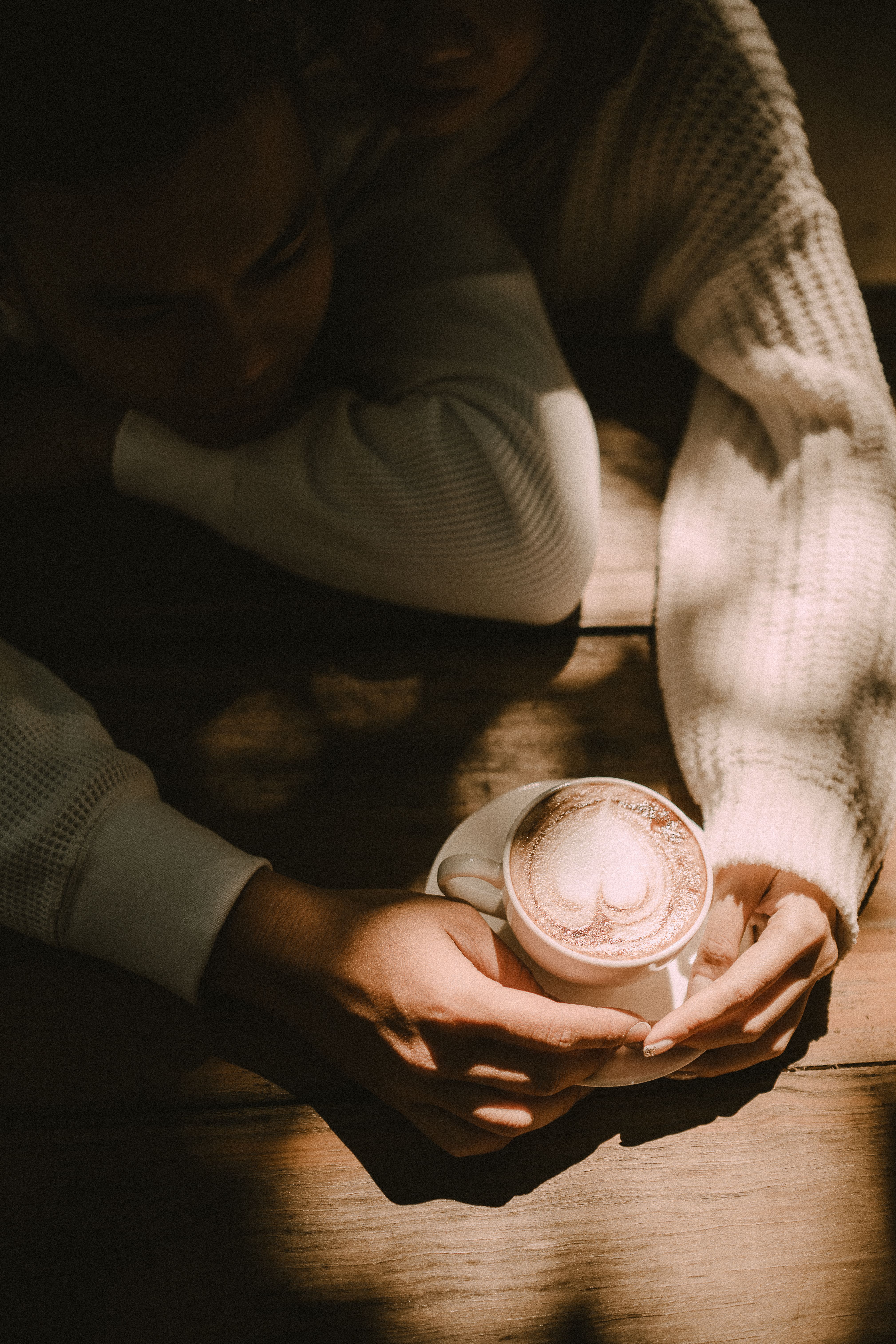 From above of crop unrecognizable couple in knitted sweaters with cup of coffee at wooden table