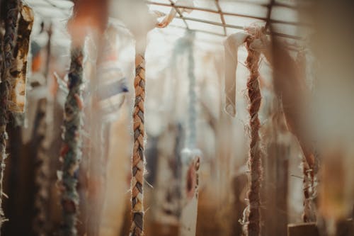 Assorted religious braided ropes with ornamental fabrics hanging on metal surface in sunlight