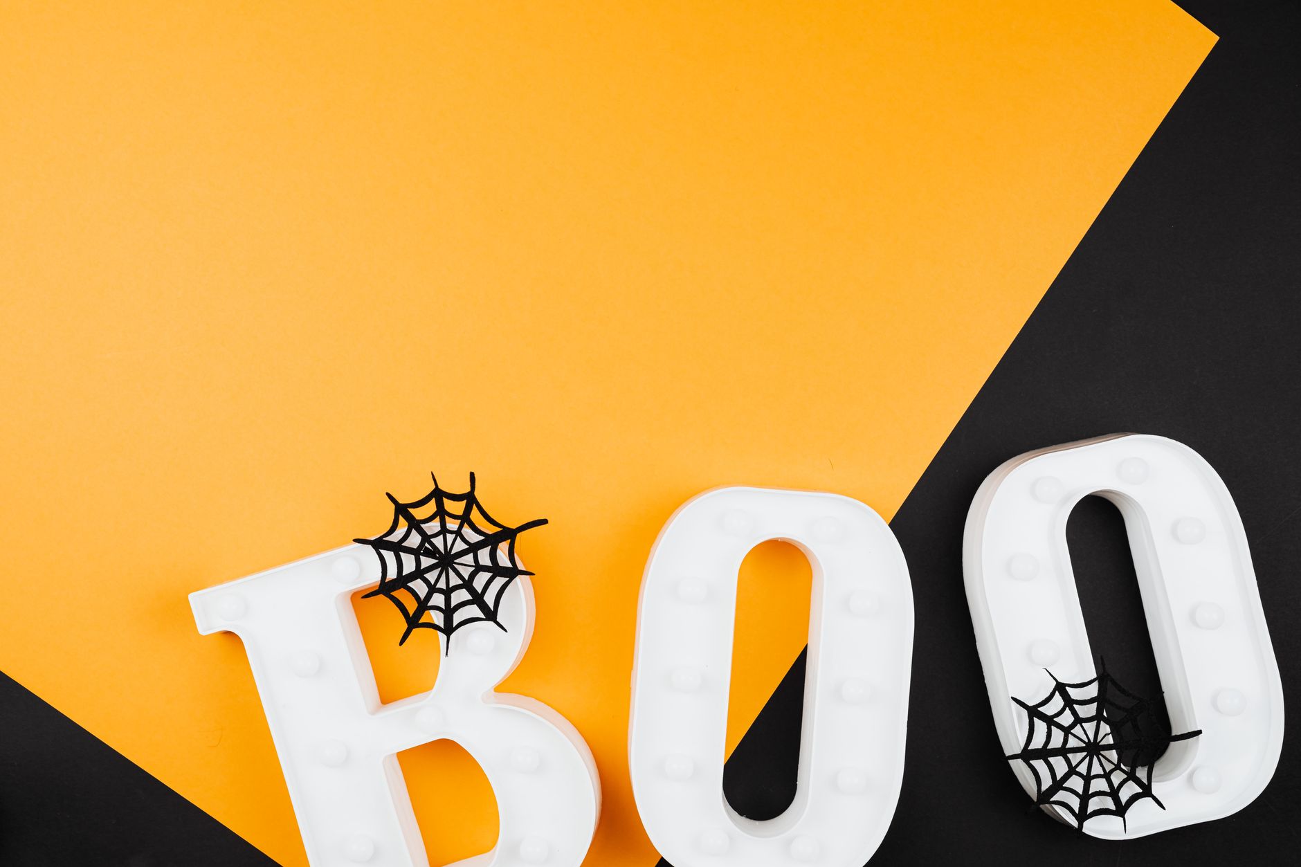 A flat lay of white 'Boo' letters with spider webs on orange and black background.