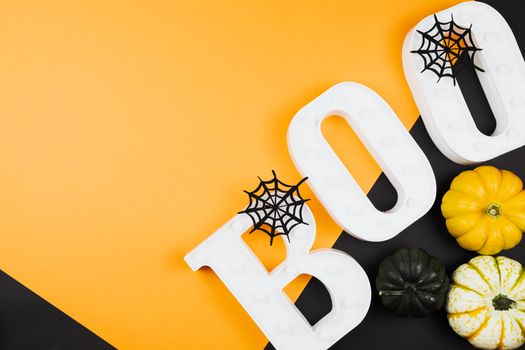 Festive Halloween arrangement with pumpkins, cobwebs, and BOO letters on orange background.