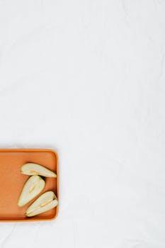 Sliced pears arranged on an orange tray with ample copy space on a white background.