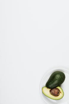 High-angle shot of a fresh avocado cut in half on a white plate with ample copy space.