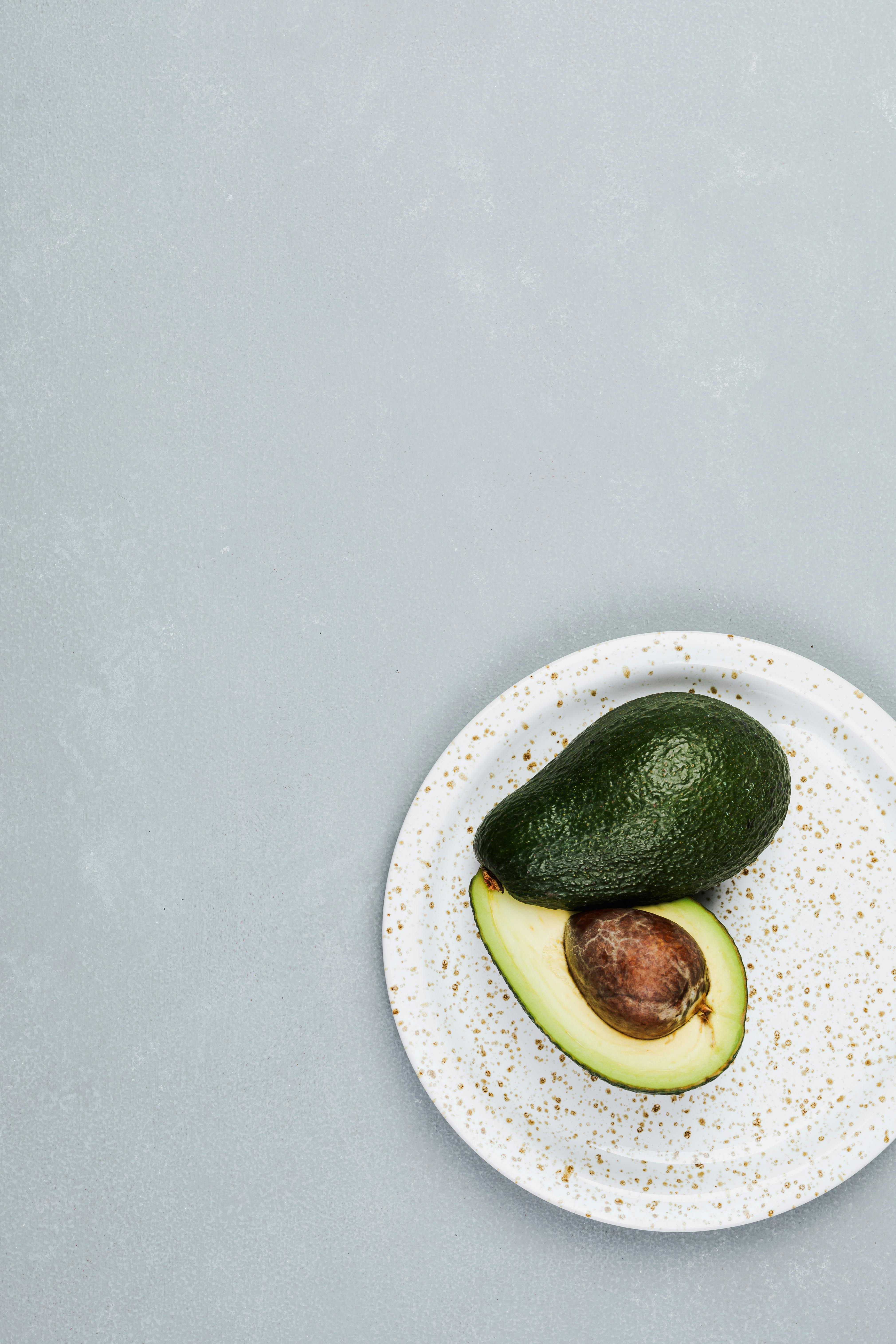 Minimalist flat lay of a whole and sliced avocado on a speckled plate with copyspace.