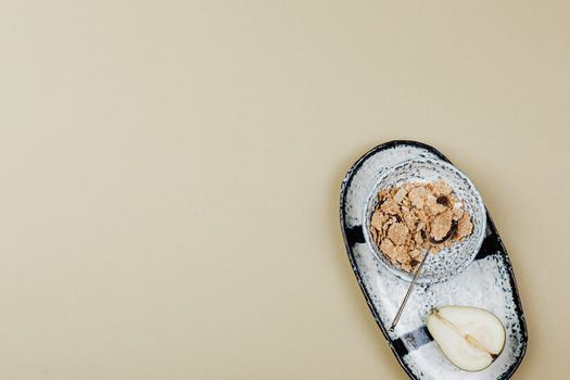 A minimalistic breakfast setting with cereal and a sliced pear on a tray with ample beige background space.