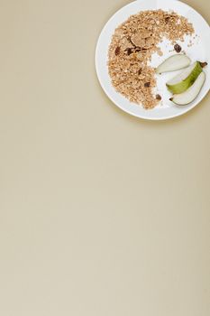 Flat lay of granola and pear slices on a white plate with a beige backdrop.