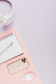 Stylish flat lay of smartphone, headphones, and notebook on pastel surface for modern tech themes.