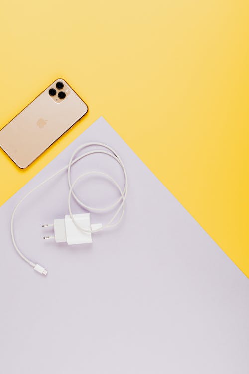 Close-Up Shot of a Mobile Phone and a Charger on a Yellow Surface