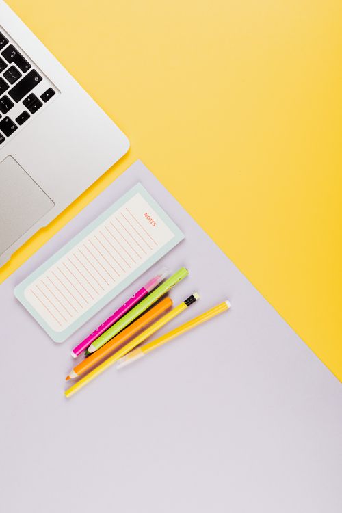 Free A flat lay of colorful stationery with a laptop on a vibrant yellow and gray desk. Stock Photo