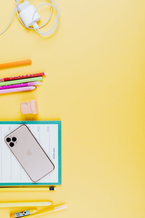 Close-Up Shot of a Smartphone beside School Supplies on a Yellow Surface