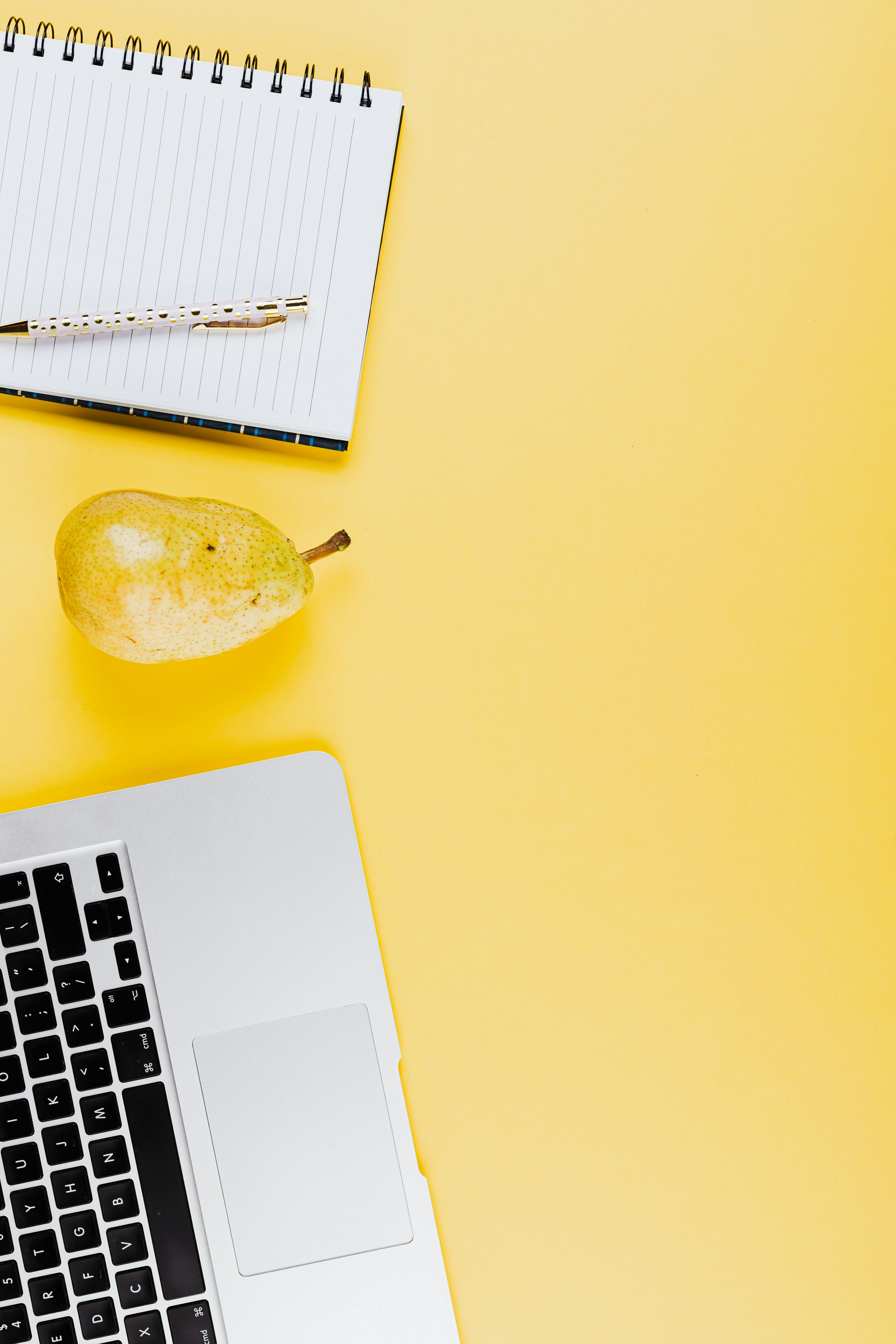pear fruit beside a spiral notebook and laptop on yellow background