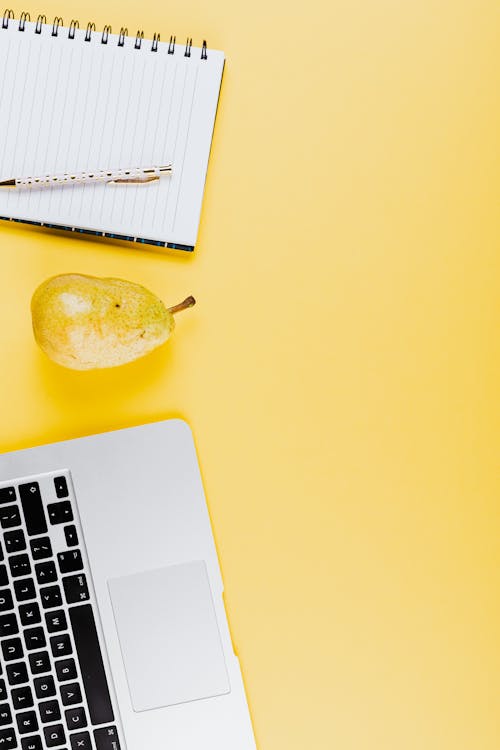 Pear Fruit Beside a Spiral Notebook and Laptop on Yellow background