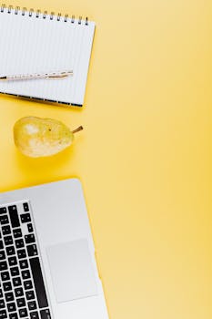 将笔记本电脑和梨平放在黄色背景上，以提供创意工作区