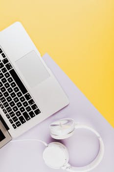 Modern flat lay of laptop and headphones on yellow and purple surface. Perfect for tech themed visuals.
