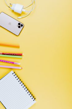 在充满活力的黄色背景上，五颜六色的扁平学校用品、电话和充电器与复制空间一同呈现