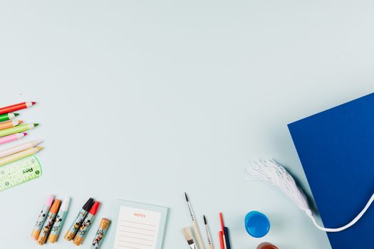 Flat lay of art supplies and graduation cap on light blue background, perfect for creative themes.